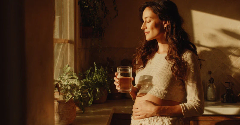 Pregnant woman drinking water in morning kitchen